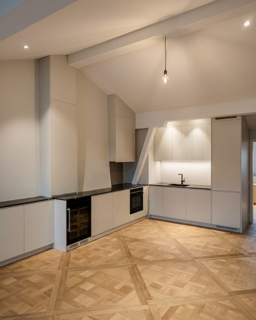 Cuisine sur mesure — façades crème mat, plan en pierre noire et parquet Versailles